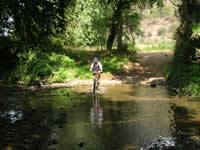 Ciclista a atravessar o rio nos trilhos do vale do lizandro a pedalar numa das nossas voltas
